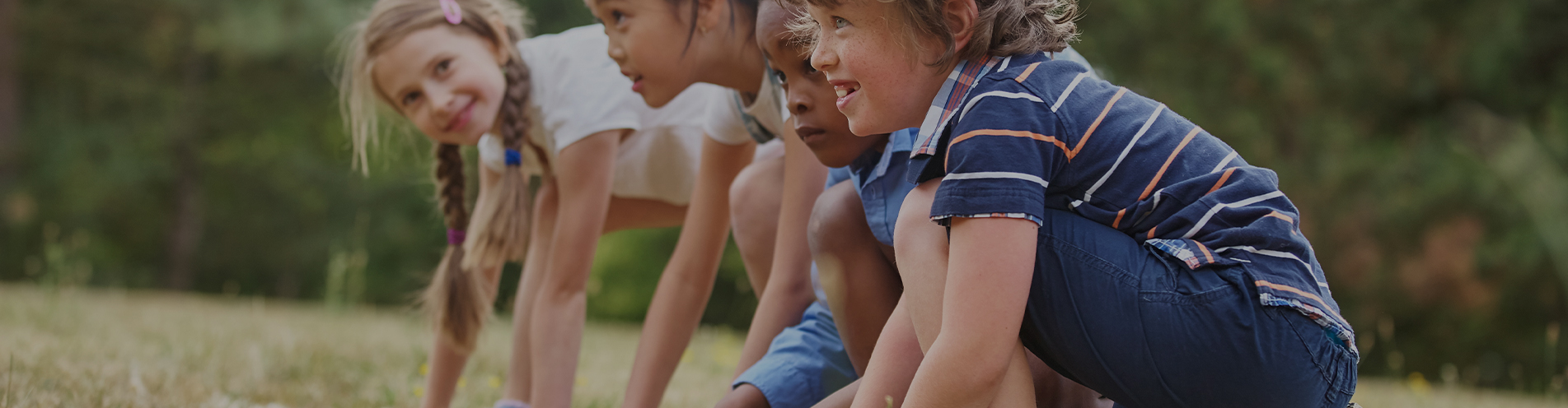 Several happy children in a line getting ready to race each other in a park