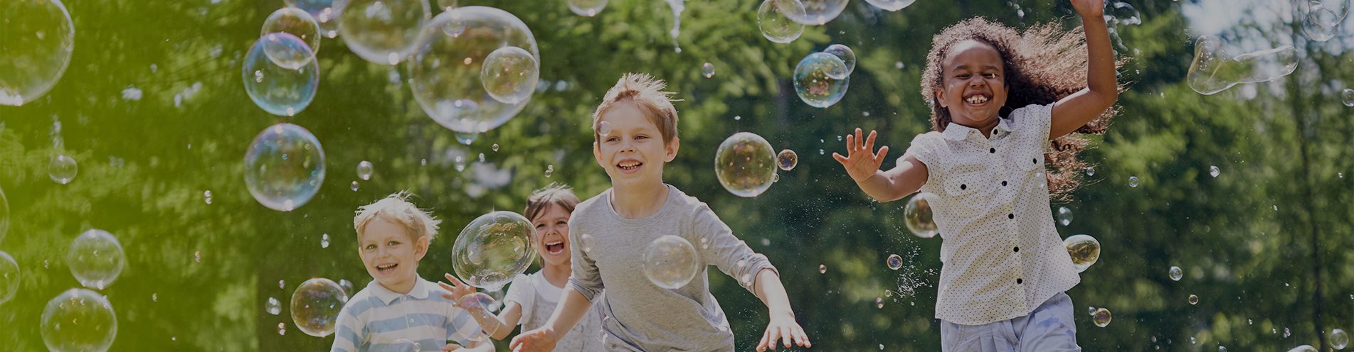 Three happy children chasing bubbles in a lush, green park on a sunny day