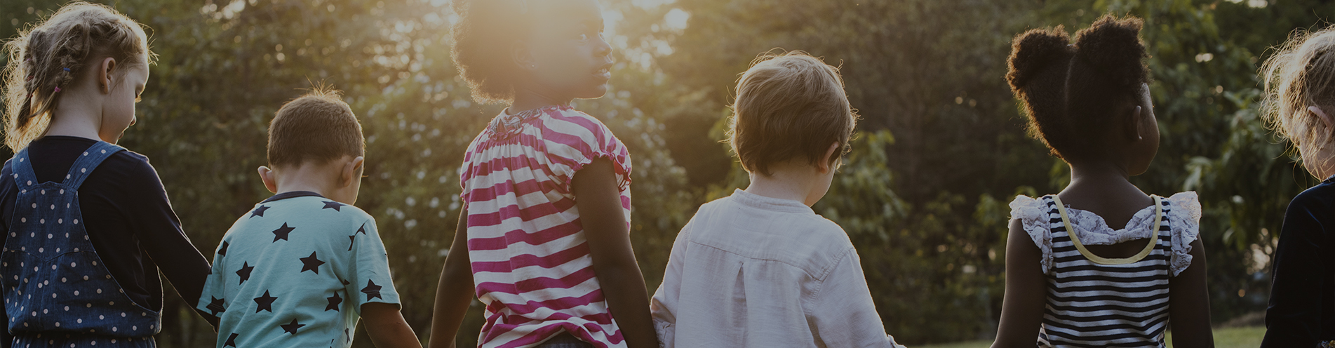 A diverse group of children standing together in a tree-filled park on a sunny day