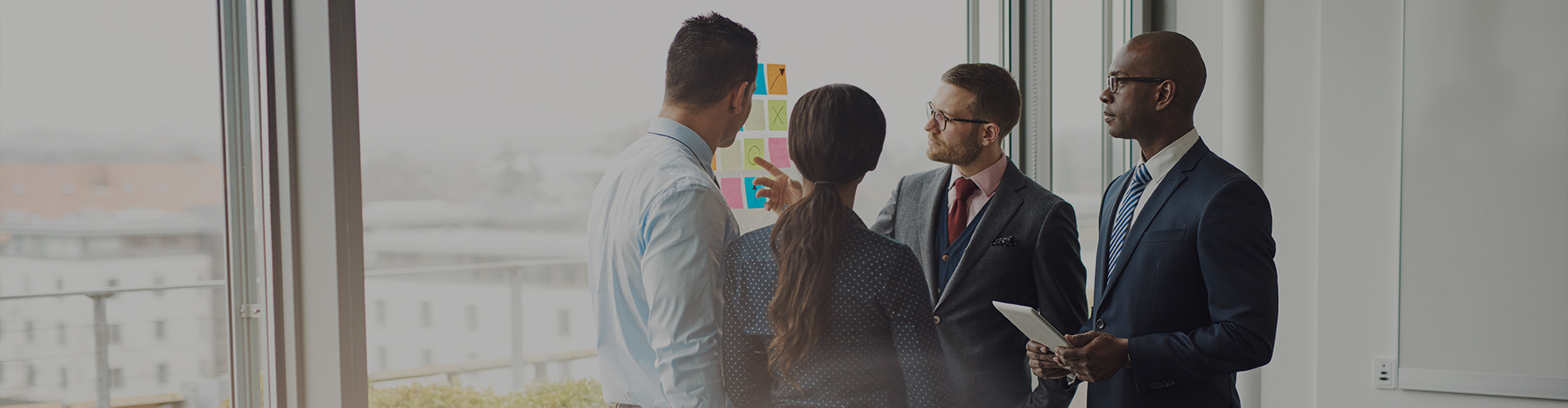 Business people in suits examine a graph overlaid on a bright office window