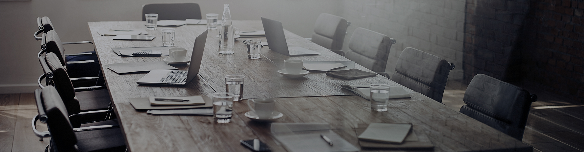 An empty corporate boardroom with long meeting table set with documents and laptop computers