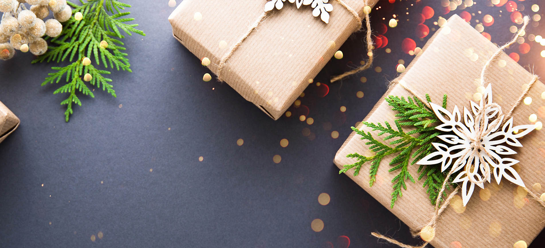 Holiday gifts wrapped in brown paper are pictured against a dark gray background with festive gold and red circles and evergreen branches.