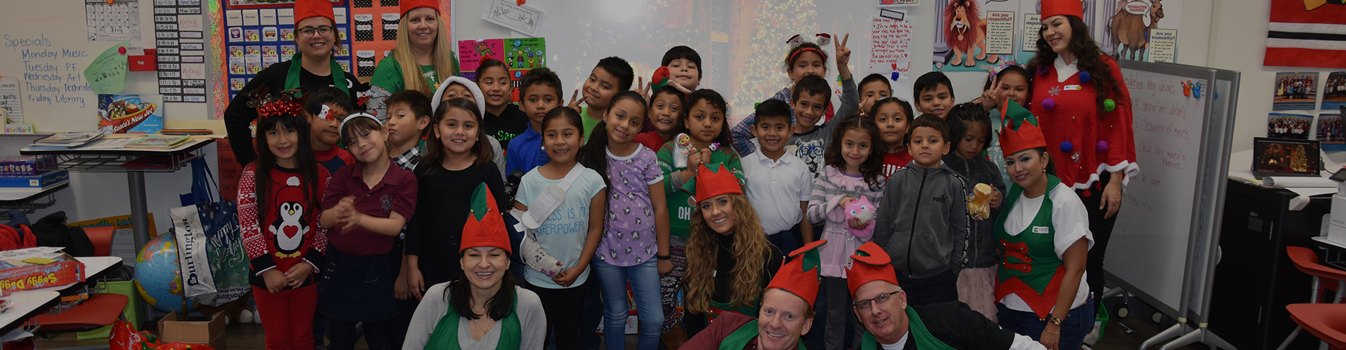 A group of happy children and volunteers in elf outfits in a classroom
